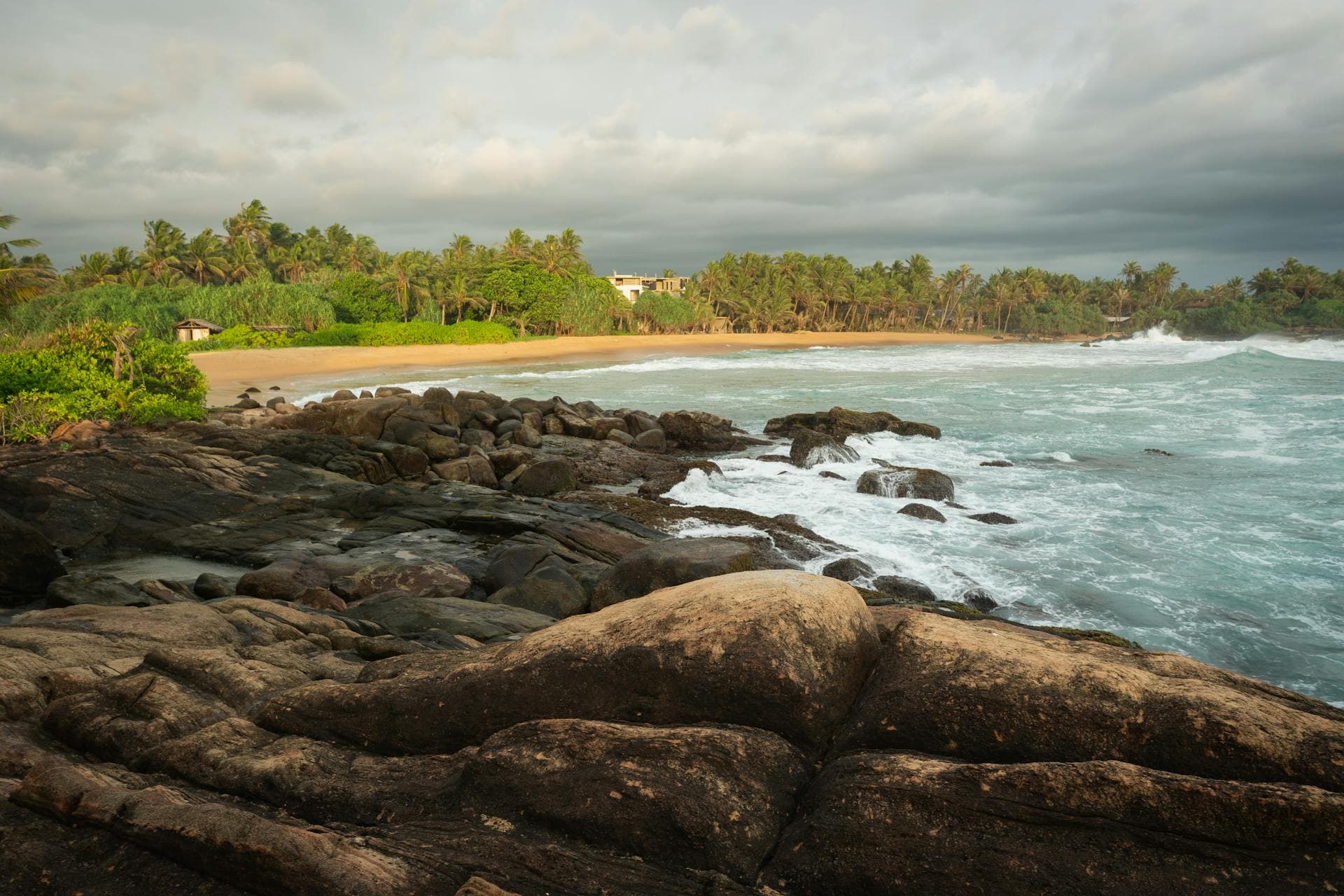 Surf rolling onto a golden palm-fringed Sri Lankan beach at sunset